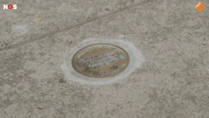 Foto van een ronde bronzen steen met een tekst over een tot slaaf gemaakte in de straat.