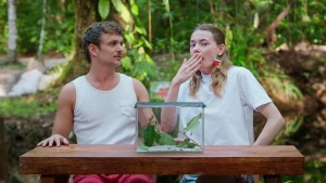 Een foto van Emma en Jurre buiten aan een tafel, beide dragen ze een wit shirt, op de tafel staat een glazen bak. Jurre kijkt naar Emma, zij houdt geschrokken een hand voor haar mond.