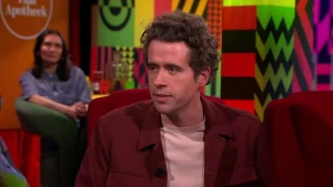 Een foto van schrijver Thomas Heerma van Voss in een rode stoel in de studio. 