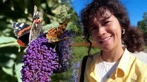 Een foto van presentatrice Serah naast een paarse plant waarop 2 vlinders zitten.