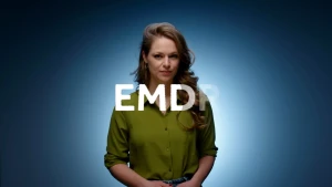 Presentatrice Sophie staat voor blauwe muur terwijl in het wit de letters EMDR voor haar verschijnen.