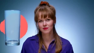 Foto van presentator Jeanine voor blauwe muur met naast haar een leeg waterglas.