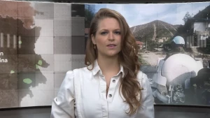 Foto van presentatrice Sophie voor een muur waarop beelden uit Srebrenica worden getoond.