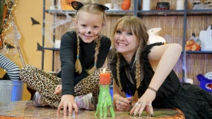 Foto van presentatrice Rosalie met meisje en zelfgeknutselde groene Frankensteinhand met kaars erop.