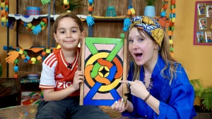 Foto van presentatrice Rosalie met meisje en zelfknutseld wandpaneel met felle kleuren.