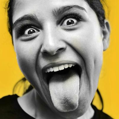 Foto van meisje op gele achtergrond dat tong uitsteekt, photo by Pedro Miguel Aires on Usplash.