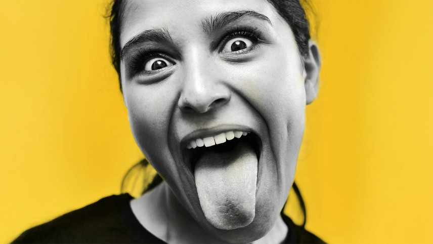 Foto van meisje op gele achtergrond dat tong uitsteekt, photo by Pedro Miguel Aires on Usplash.