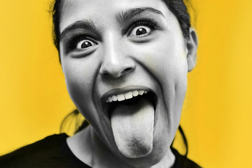 Foto van meisje op gele achtergrond dat tong uitsteekt, photo by Pedro Miguel Aires on Usplash.