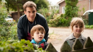 Een man en twee kinderen kijken over de bosjes heen. 