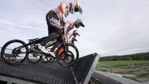 Een foto van vier mensen op kleine crossfietjes van opzij gezien. Ze staan op de pedalen, klaar voor de start. Ze dragen helmen en wedstrijdkleding.