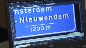 Een foto van een computerscherm waarop een ontwerpprogramma openstaat. Op het scherm is 'Amsterdam' en 'Nieuwendam' te lezen op het ontwerp van een bewegwijzeringsbord, eronder staat 1200m.