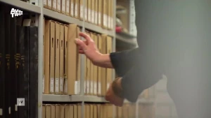 Een foto van een hand die een map uit een archiefkast pakt.