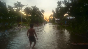 Jongetje staat met voeten in het water. Op de achtergrond palmbomen.