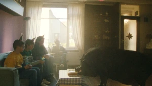 Een aantal kinderen zitten op een bank in een woonkamer. Tegenover hen een varken dat van tafel eet.