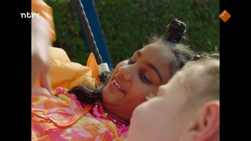 Twee meisjes liggen in het gras. Eén hindoestaans meisje en één wit meisje.