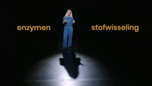 Janouk staat in een zwarte zaal met een zwarte achtergrond met twee woorden naast zich: enzymen en stofwisseling