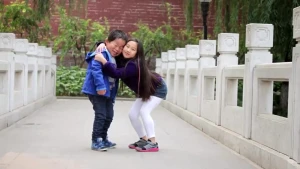 Twee kinderen, een jongen en een meisje, staan op een brug. Het meisje knuffelt de jongen.