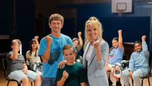 Jurre Geluk en Lars staan met Anne-Mar. Op de achtergrond zitten kinderen. Iedereen heeft een gebalde vuist met stippen erop.