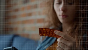 Een foto van een vrouw met een stripje pillen in haar hand, in haar andere hand heeft ze een telefoon.