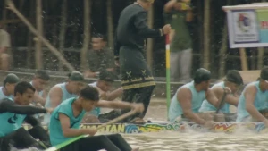 Indonesische roeiers racen op het water. Bovenop een boot staat een man in traditionele kleding.