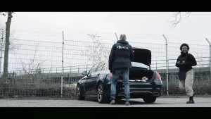 Thirsa draagt een kogelvrij vest en staat met een blij gezicht naast de politieauto, samen met een rechercheur.