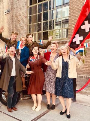 Een foto van blije mensen op straat in kleding uit de jaren 40, ze zwaaien met Canadese en Amsterdamse vlaggen.