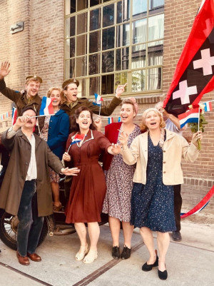 Een foto van blije mensen op straat in kleding uit de jaren 40, ze zwaaien met Canadese en Amsterdamse vlaggen.