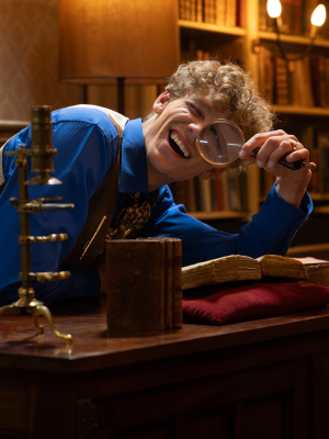 Een foto van presentator Roeland die een vergrootglas voor zijn oog houdt.