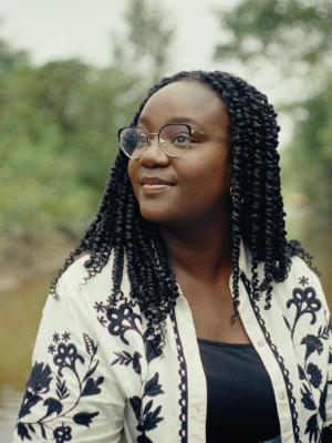 Een foto van presentator Tirsa in Suriname, ze is op het water, achter haar zie je een rivier en begroeiing op de kanten.