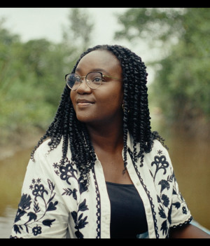 Een foto van presentator Tirsa in Suriname, ze is op het water, achter haar zie je een rivier en begroeiing op de kanten.