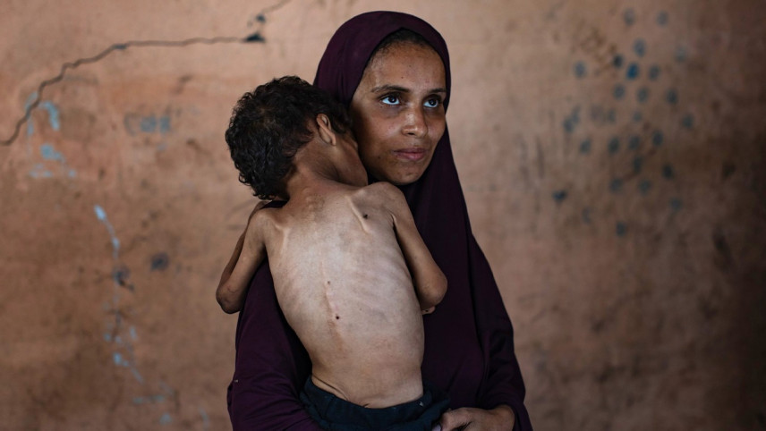 Foto van gesluierde vrouw met een mager kind op haar arm, gezien op de rug. 