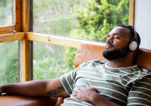 Foto van jongeman die ontspannen op de bank ligt met een koptelefoon op zijn oren en zijn ogen gesloten.