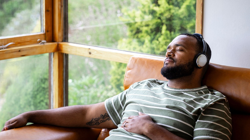 Foto van jongeman die ontspannen op de bank ligt met een koptelefoon op zijn oren en zijn ogen gesloten.