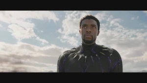 Een foto van de superheld Black Panther, een zwarte man. Hij heeft een strak zwart superheldenpak aan met paarse elementen.