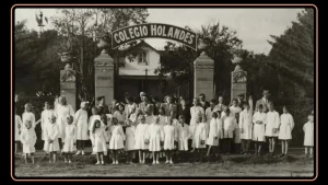 Een zwart-wit foto van een hollandse school in Argentinië, de kinderen staan in witte kleding voor de poort.
