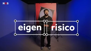 Een foto van presentator Devran in een studio. Hij kijkt in de camera. Voor hem staan groot de woorden 'eigen risico'. De studio is blauw uitgelicht en achter hem staat een poster van een vakje op een stembiljet.