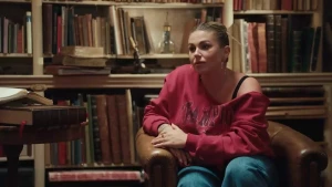 Een foto van Roxanne Hazes in een grote bruine stoel voor een kast met boeken.