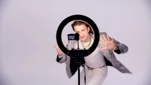 Foto van zanger in witte kleding voor selfielamp met telefoon.