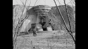 Zwart-wit beeld van een grote bunker. Voorlangs lopen twee soldaten.
