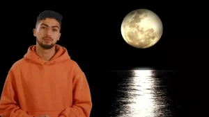 De presentator (man) is te zien met op de achtergrond een maan waarvan het licht op de zee weerspiegelt.