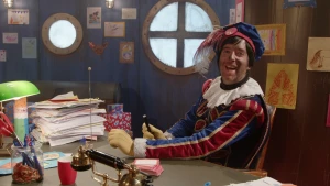 Hoofdpiet kijkt lachend in de camera van achter zijn bureau.