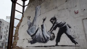 Foto van een graffitikunstwerk van Banksy, twee judoende kinderen waarbij de een de ander op de grond gooit, afgebeeld op een afbrokkelende muur.