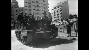 Een tank met daarop soldaten rijdt door een straat.