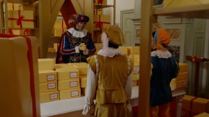 Hoofdpiet spreekt Pieten toe in de Pakjeskamer. Ze zijn omringd door noodpakketten.