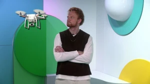 Een foto van Sil in de studio, hij kijkt met zijn armen over elkaar naar een drone die bij zijn gezicht vliegt.