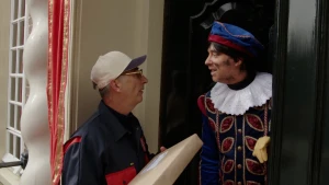 Hoofdpiet staat in de deuropening, voor de deur staat de postbode met een pakketje.