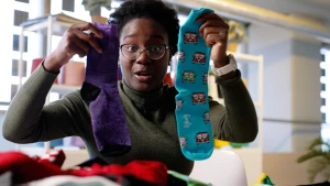 Foto van presentatrice Tirsa die twee sokken omhoog houdt, een paarse en een blauwe met gekleurde volkswagenbusjes.