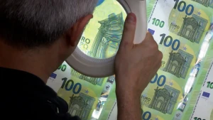 Foto van man die reeks eurobiljetten van 100 euro bekijkt door vergrootglas.