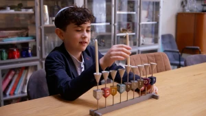 Foto van joodse jongen met donker haar en keppeltje op zijn hoofd aan een tafel met daarop een achtarmige kandelaar, de chanoekia.