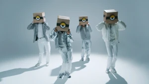 Foto van vier in het wit en zilver geklede jongens met een kartonnen doos op hun hoofd waarop een oog van een minion staat.